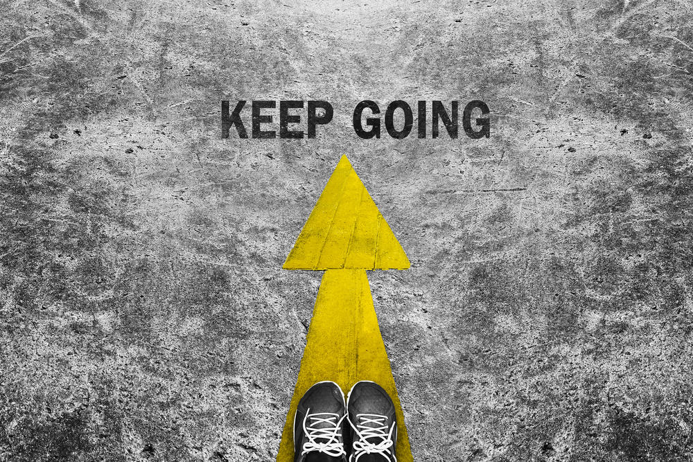Two feet on concrete ground with yellow arrow pointing forward and the words "keep going."