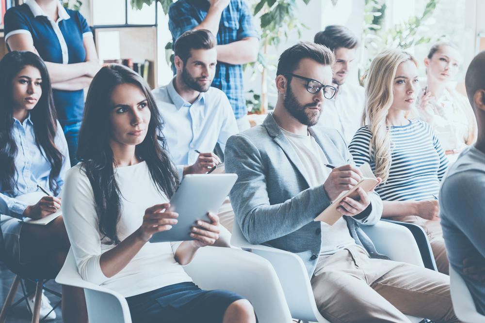 Group of young professionals sitting in conference together and taking notes.