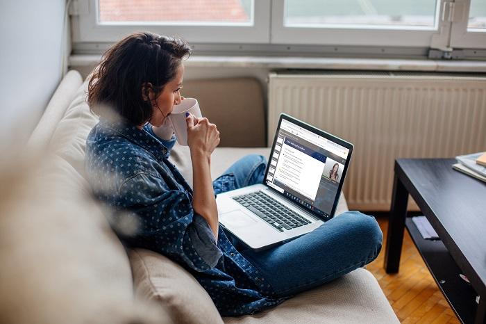 a woman looks at the Becker site on a couch on a laptop while drinking from a mug