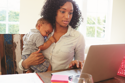 Woman holding child and working on laptop