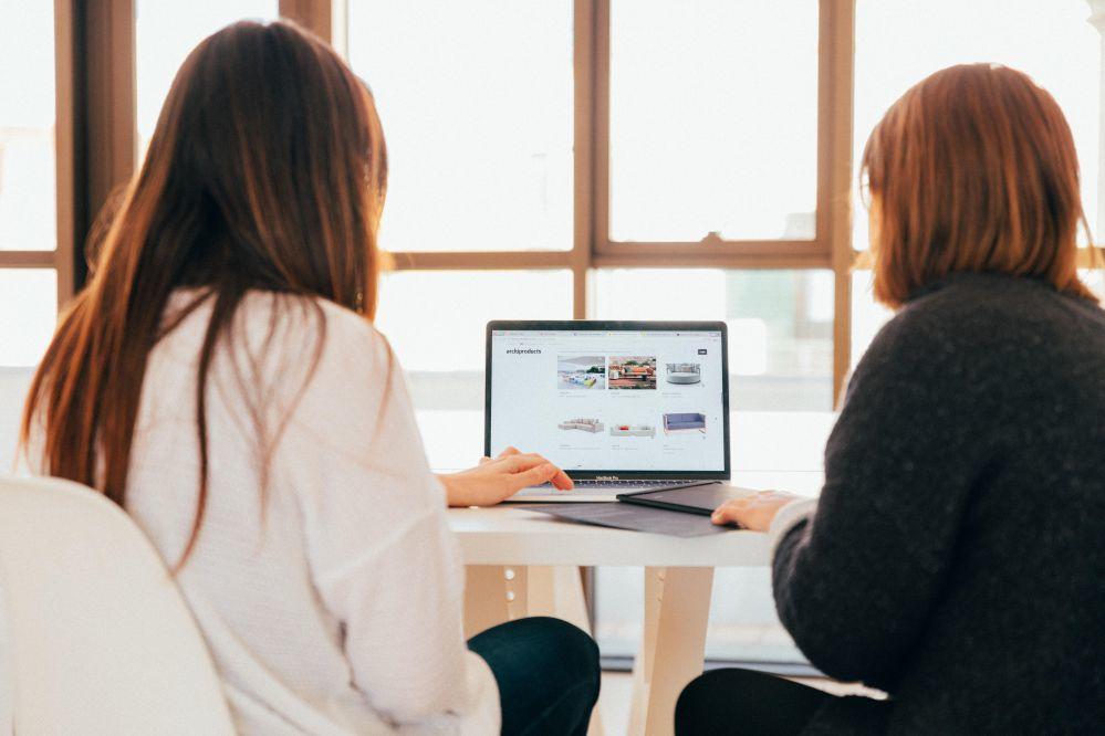 two women work on a laptop