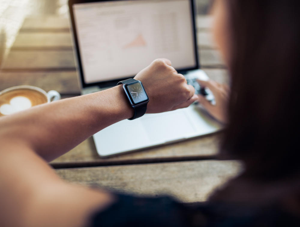 person looking at watch while using laptop