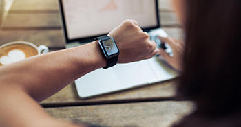 Student looking at their wristwatch with a laptop in the background