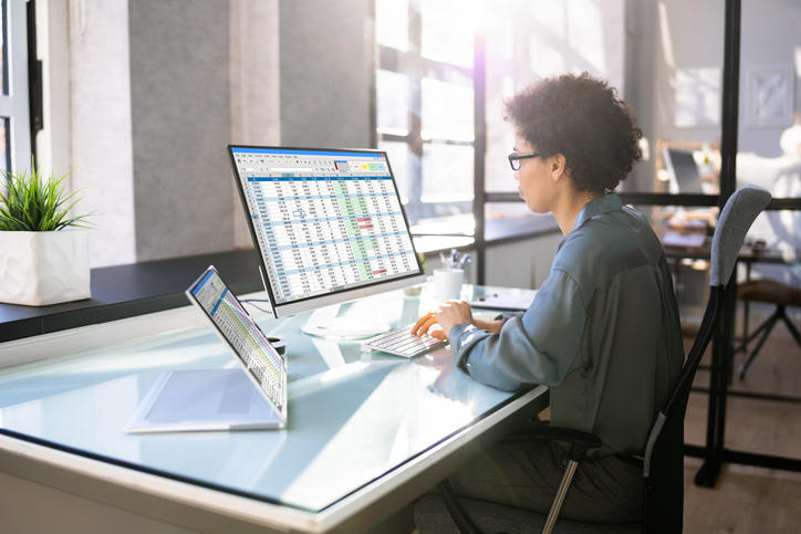 person working at two computer screens with spreadsheets