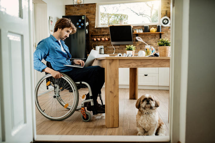 person in wheelchair working on laptop with their dog