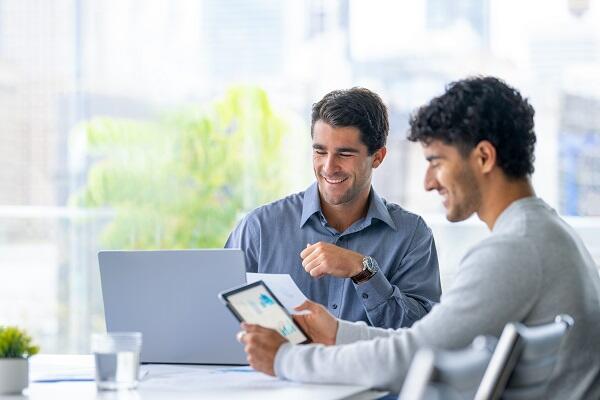 Two men in their 30s sitting at a conference table and discussing tax law harvesting