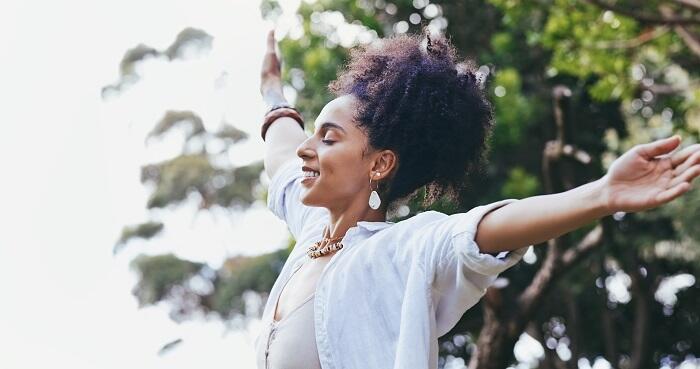 A young Black woman in a white shirt looking peaceful, standing in the sun with her arms outstretched and prioritizing her mental health while preparing for the CPA Exam.