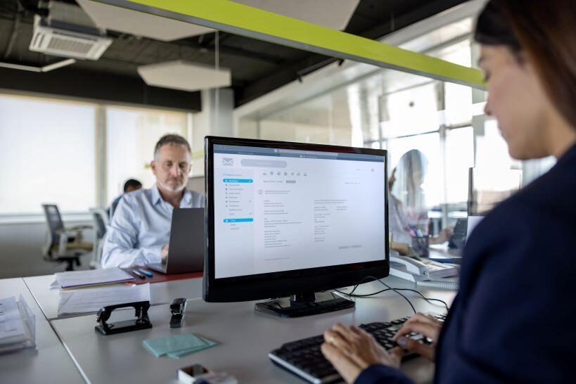 Over-the-shoulder view of a woman working at a computer screen researching the risks of AI in accounting. 