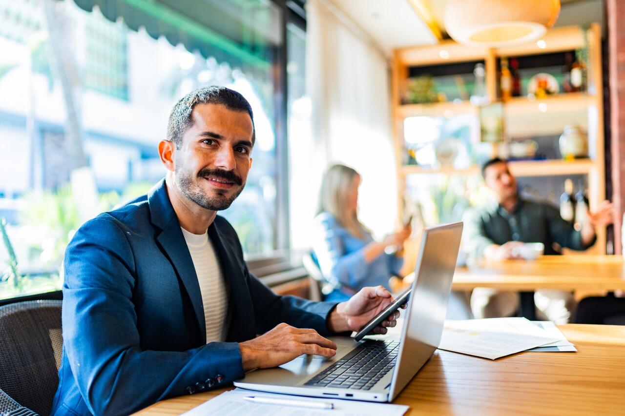 man at a desk on a laptop with others nearby at desks