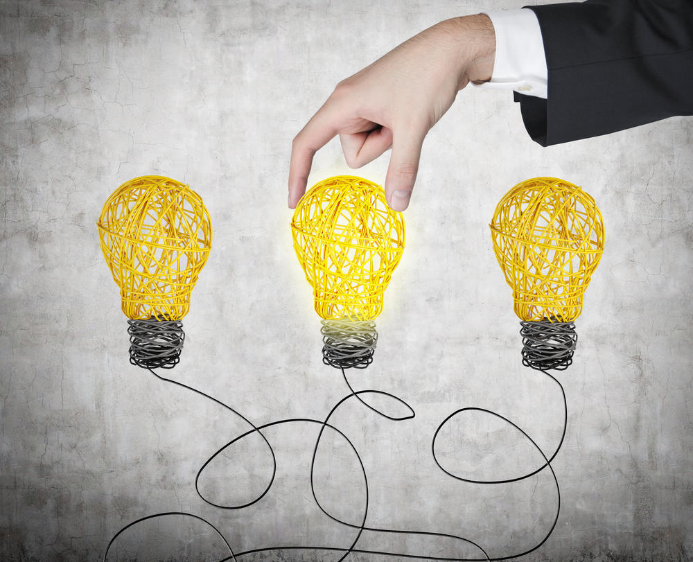 A hand chooses one light bulb out of three others. A metaphor of the right decision.
